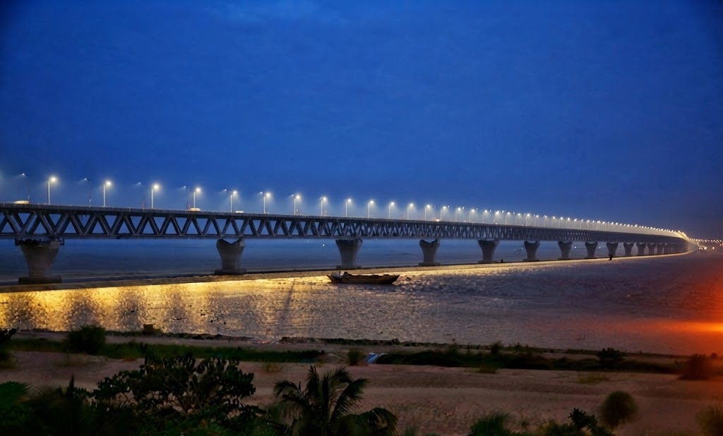 Glowing under a deep twilight blue sky with its golden reflection on the Padma River